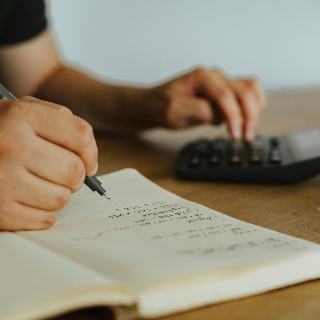 A man focused on budget planning, writing in a notebook with a pen and using a calculator for financial calculations.